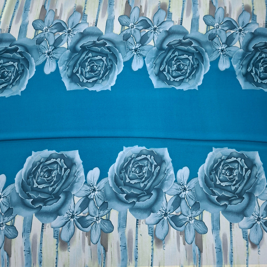 A close-up of a blue fabric or wallpaper pattern featuring large blue-gray roses and small star-like flowers, with vertical brushstroke accents in off-white and beige.
